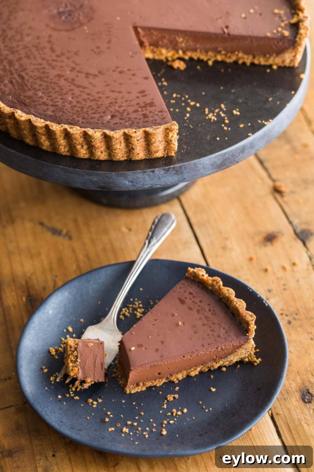 A single slice of chocolate tart on a black plate with silver fork.