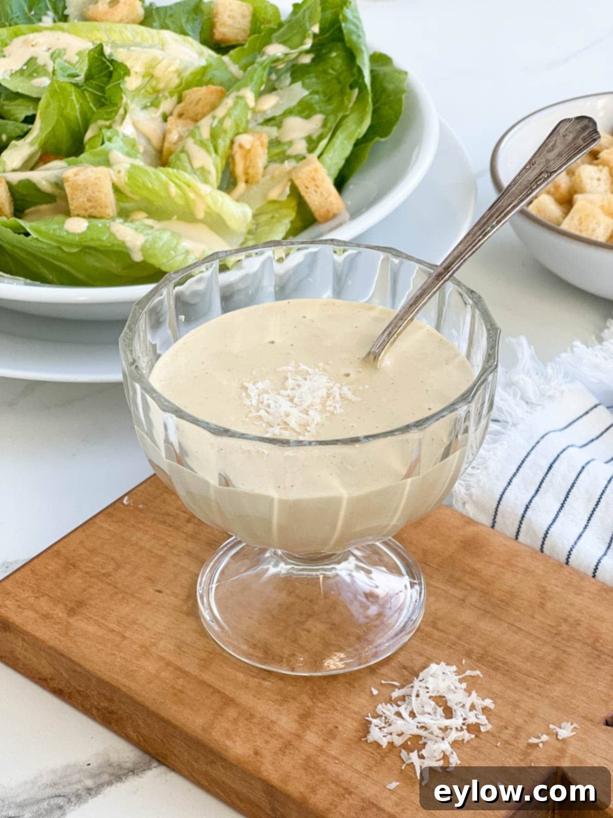 Caesar Dressing No Anchovies Needed 2 A glass bowl filled with rich, creamy homemade Caesar dressing, garnished with a spoon and fresh lemon slices.
