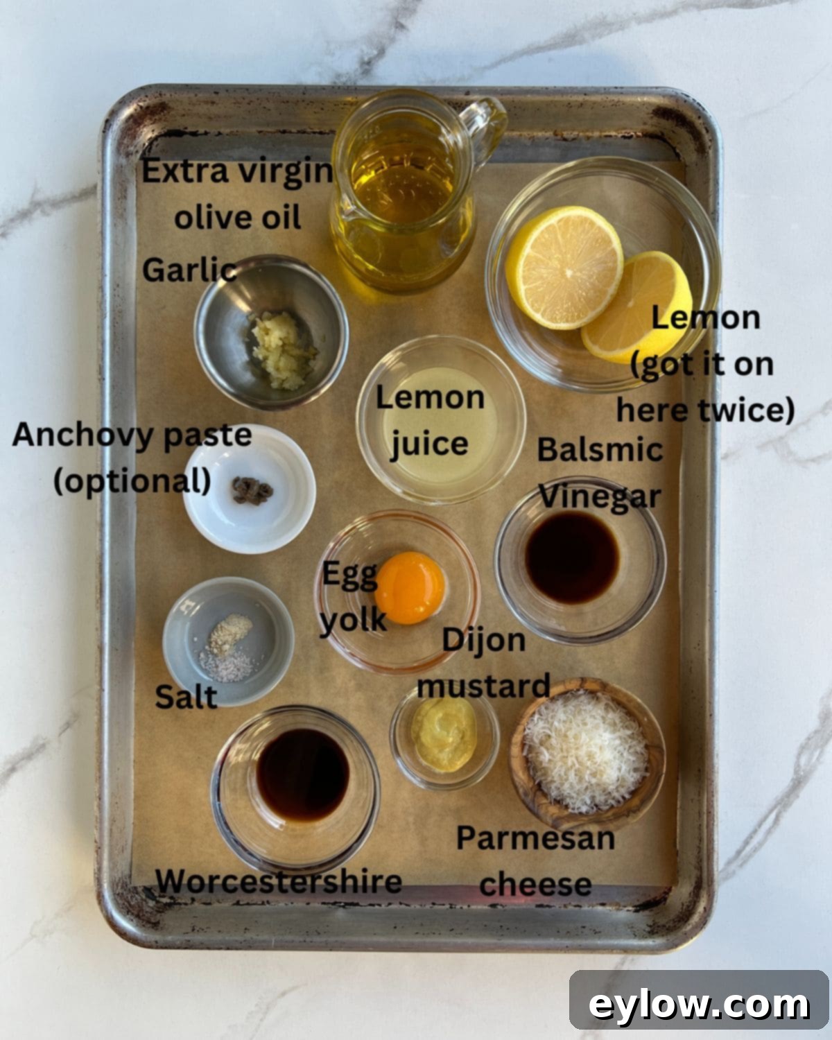 Caesar Dressing No Anchovies Needed 3 Assorted Caesar salad dressing ingredients laid out in small ceramic bowls, including lemon halves, an egg yolk, Dijon mustard, garlic cloves, olive oil, and Parmesan cheese.