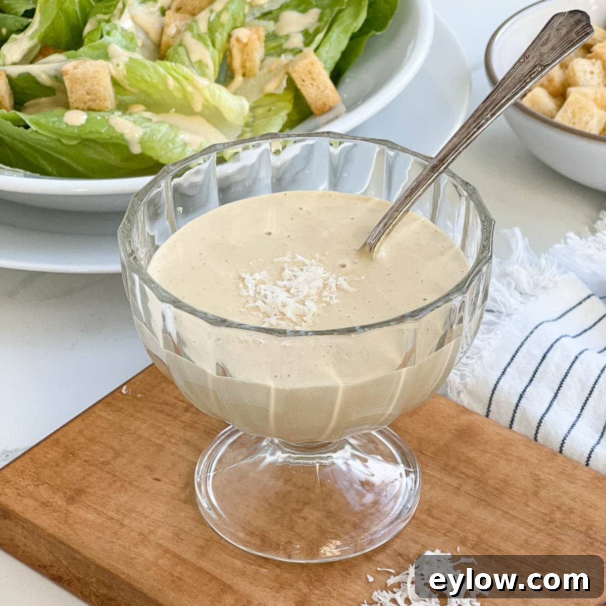Caesar Dressing No Anchovies Needed 4 A close-up of a glass bowl filled with creamy Caesar dressing, with a silver spoon resting inside.