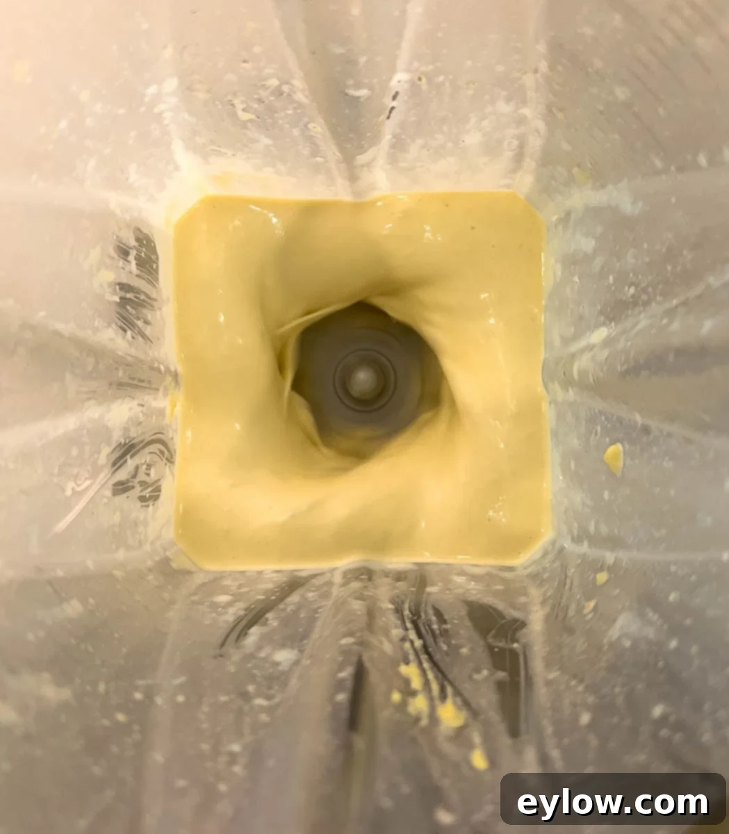 Caesar Dressing No Anchovies Needed 6 Blender with creamy caesar dressing, showing the process of pouring oil into the running blender for emulsification.