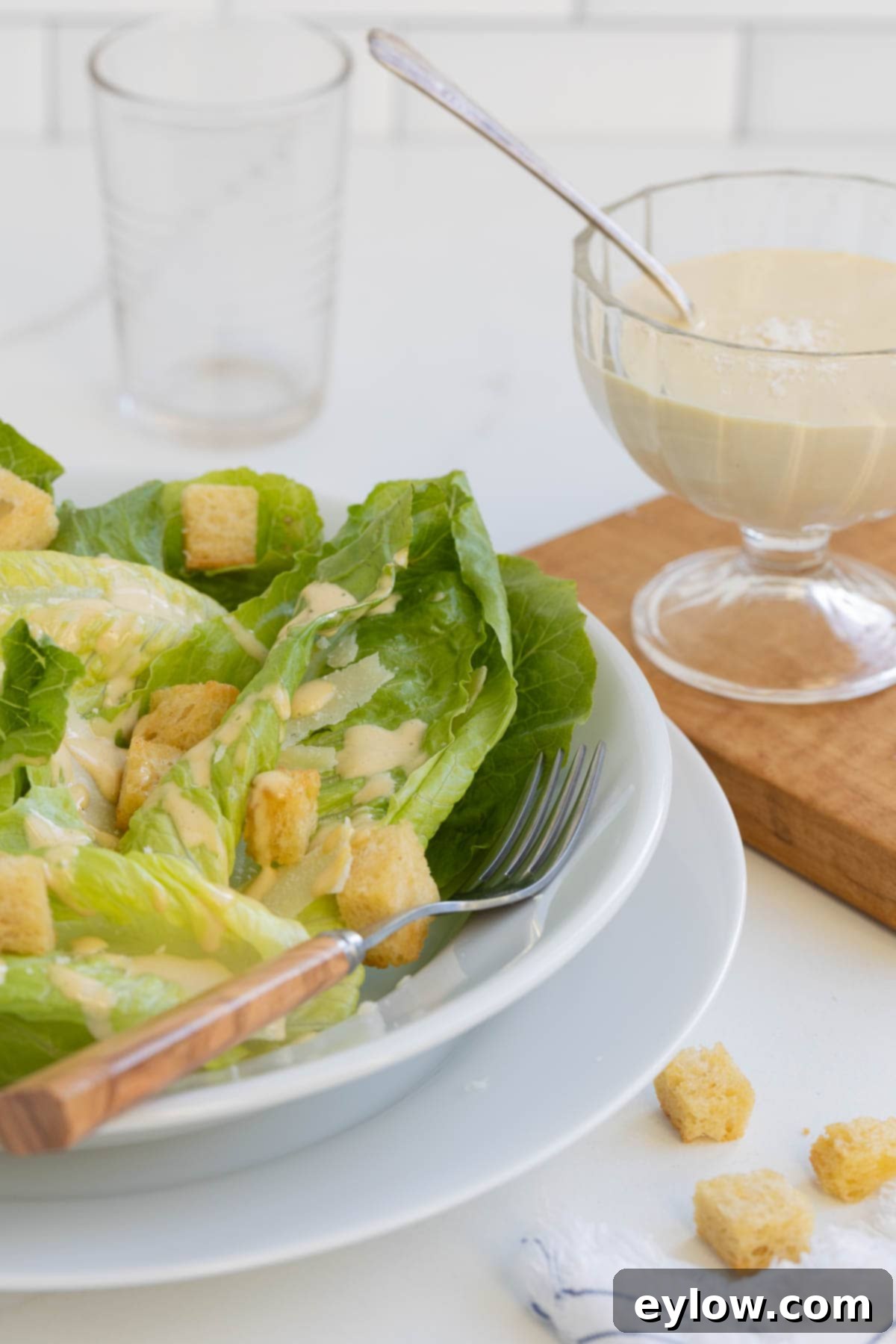Caesar Dressing No Anchovies Needed 8 A large bowl of Caesar salad with crisp romaine lettuce and croutons, accompanied by a small glass bowl of homemade Caesar dressing on the side.