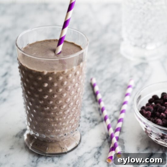 A chocolate blueberry smoothie in a glass with purple striped straws and blueberries beside, suggesting a refreshing and healthy drink.
