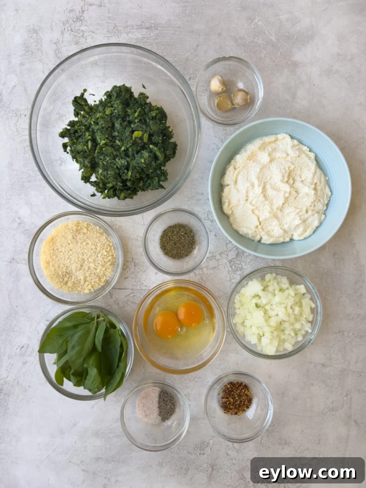 Fresh ingredients laid out for creamy ricotta filling: spinach, ricotta, Parmesan, eggs, onion, garlic, and herbs.