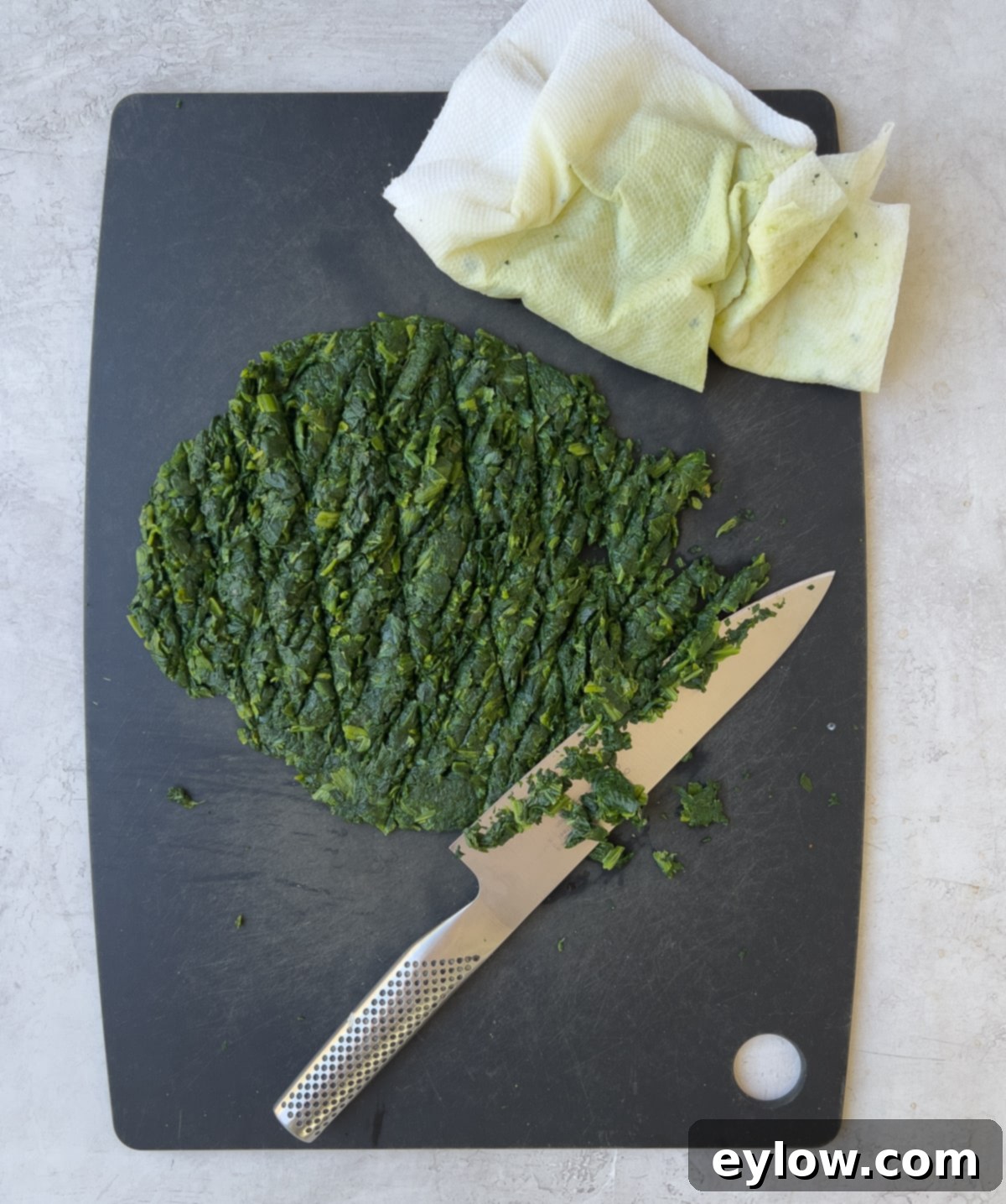 Finely chopped cooked spinach on a cutting board, ready to be incorporated into the ricotta filling.