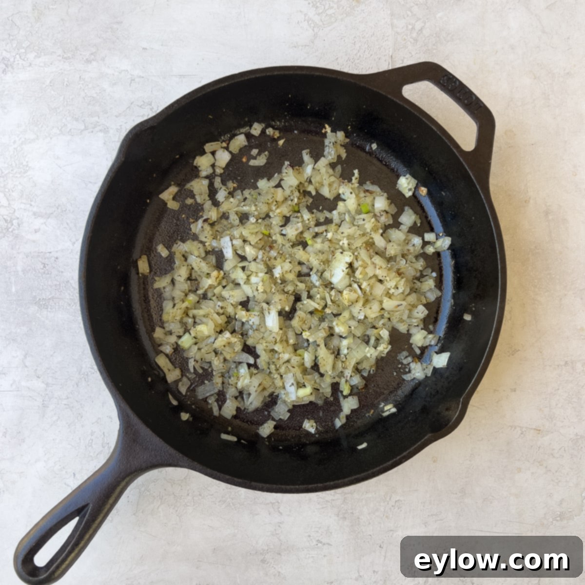 Sautéing chopped onions in olive oil in a cast iron pan, forming an aromatic base for the filling.