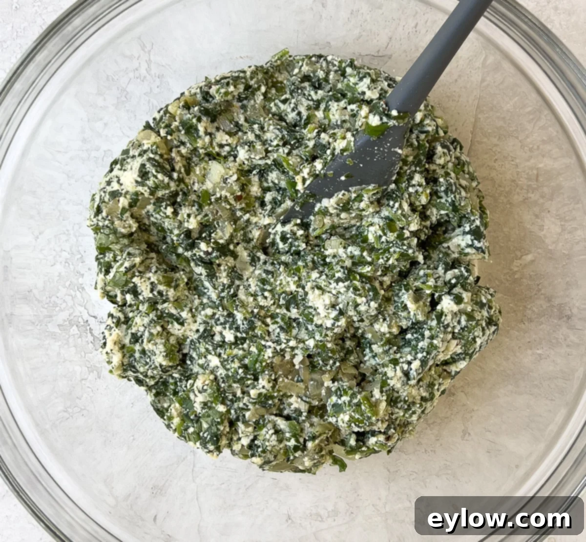 A large glass bowl filled with the perfectly prepared creamy spinach ricotta filling, garnished with a sprig of basil.