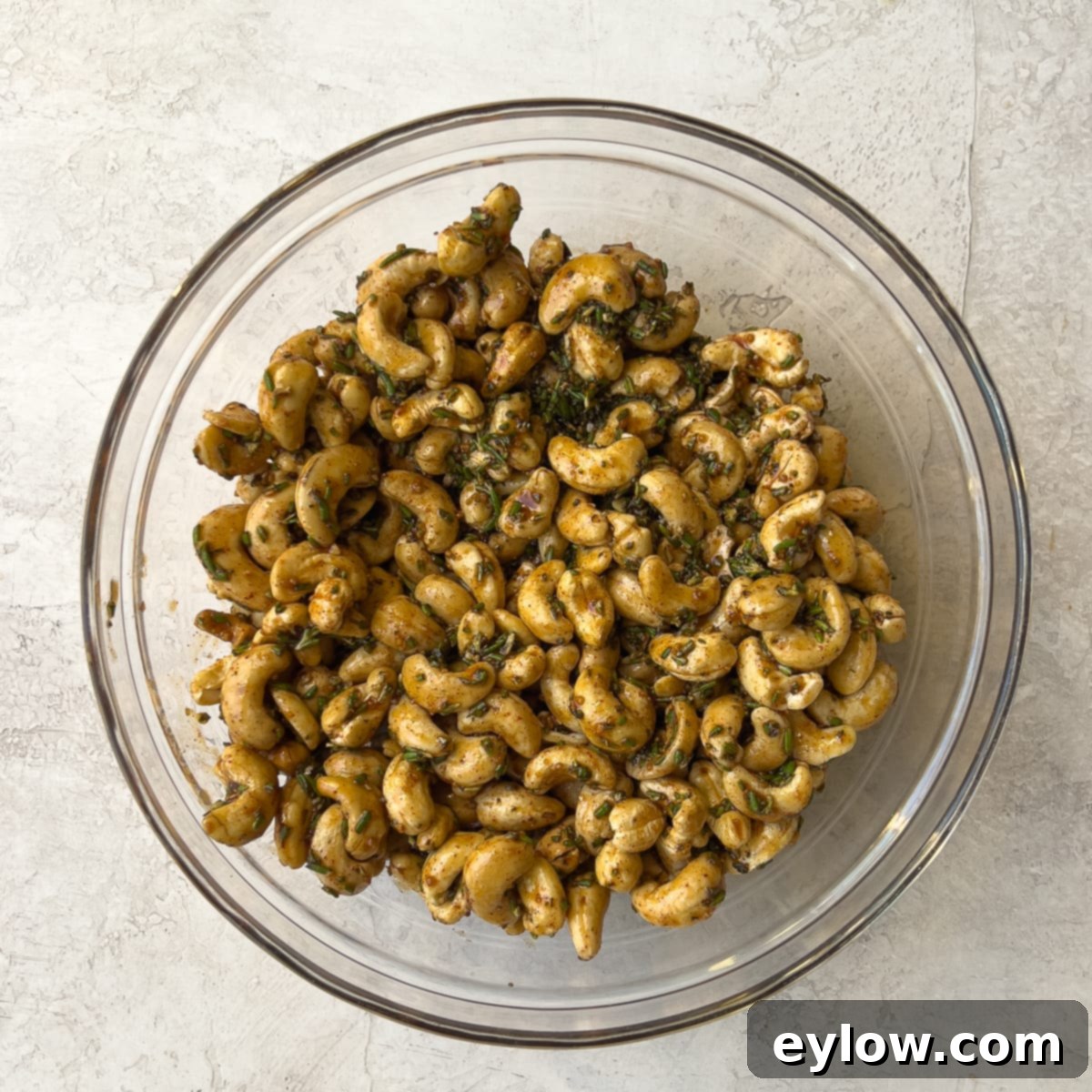 Maple Glazed Sweet and Spicy Cashews 5 Cashews mixed with maple syrup and spices. Raw cashews are coated in a dark, glossy maple and spice mixture in a mixing bowl.