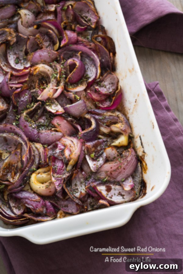 A white casserole dish filled with perfectly roasted purple red onion wedges, glistening with balsamic glaze and sprinkled with fresh herbs.