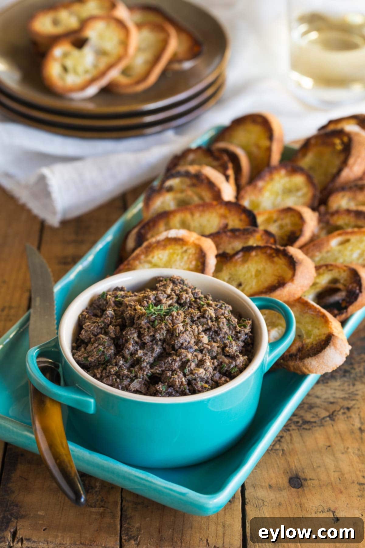 A small blue bowl of mushroom duxelles with crisp crostini on a platter.