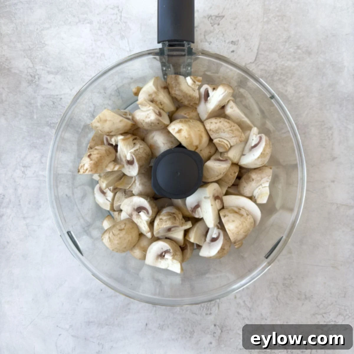 Adding quartered mushrooms to a food processor workbowl.