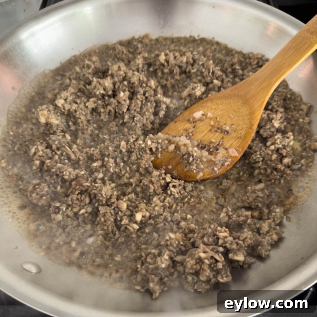 Chopping mushroom cooking for duxelles in a fry pan.