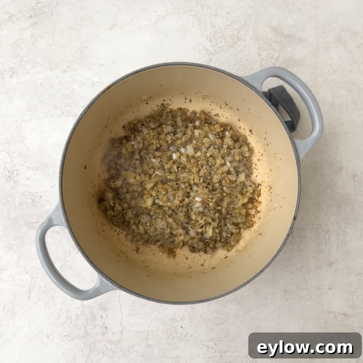 Dried herbs being stirred into the moist onions and garlic in a Dutch oven.