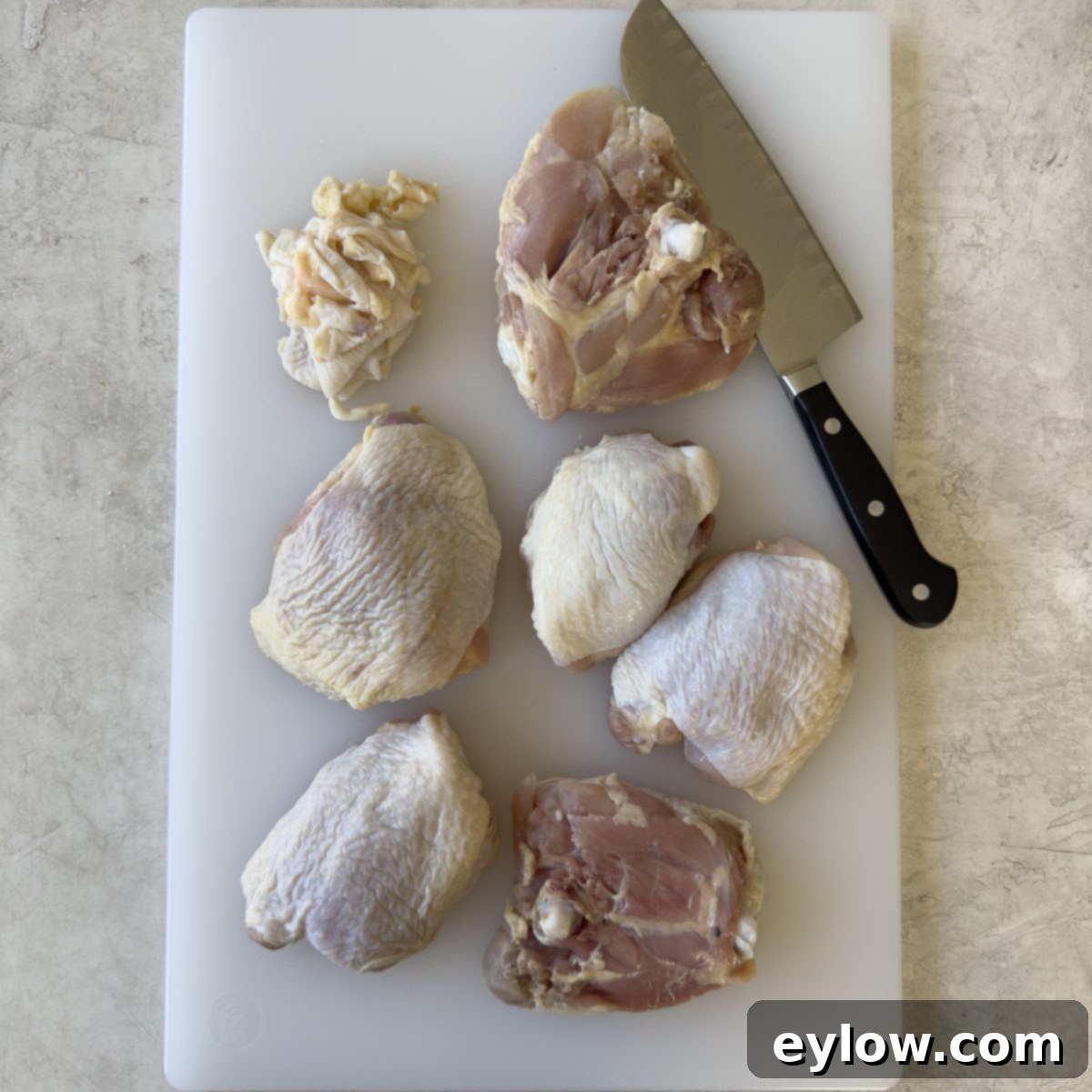 Effortless One Pan Italian Chicken Thighs 4 Trimming chicken thighs of extra far on a cutting board.