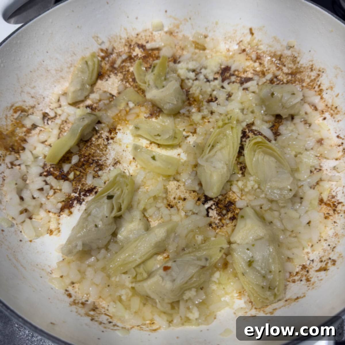 Effortless One Pan Italian Chicken Thighs 7 Adding onion, garlic, and artichoke hearts to the pan to make a sauce.