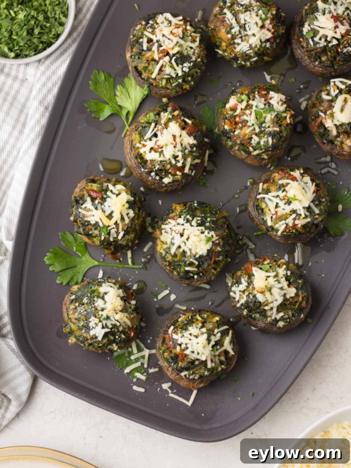 A grey platter filled with beautifully arranged spinach stuffed mushrooms, garnished with fresh parsley and melted Parmesan cheese.
