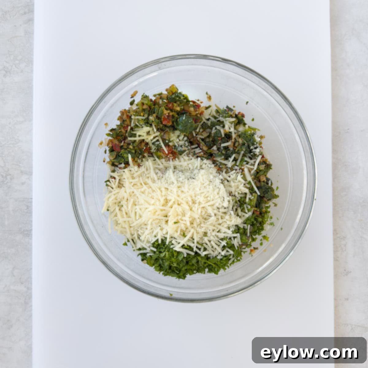 A glass bowl containing the fully cooked and cooled stuffing mixture for spinach stuffed mushrooms, mixed with Parmesan cheese and parsley.