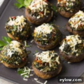A serving plate showcasing perfectly baked spinach stuffed mushrooms, topped with melted Parmesan cheese and fresh parsley.
