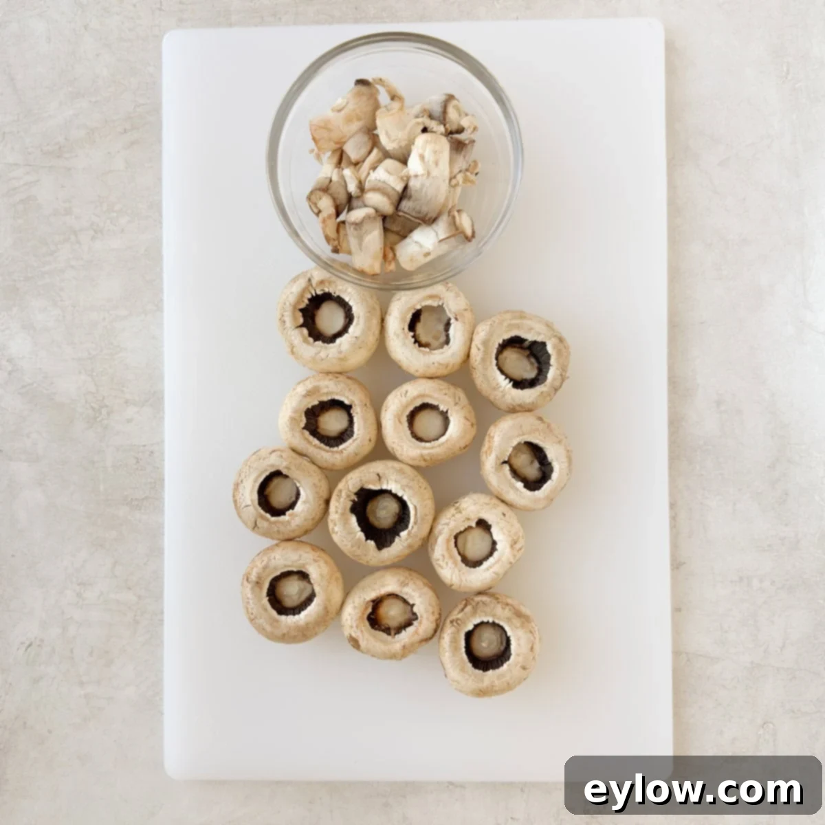 Mushroom caps arranged top-down on a cutting board, with their stems removed and reserved for the filling.