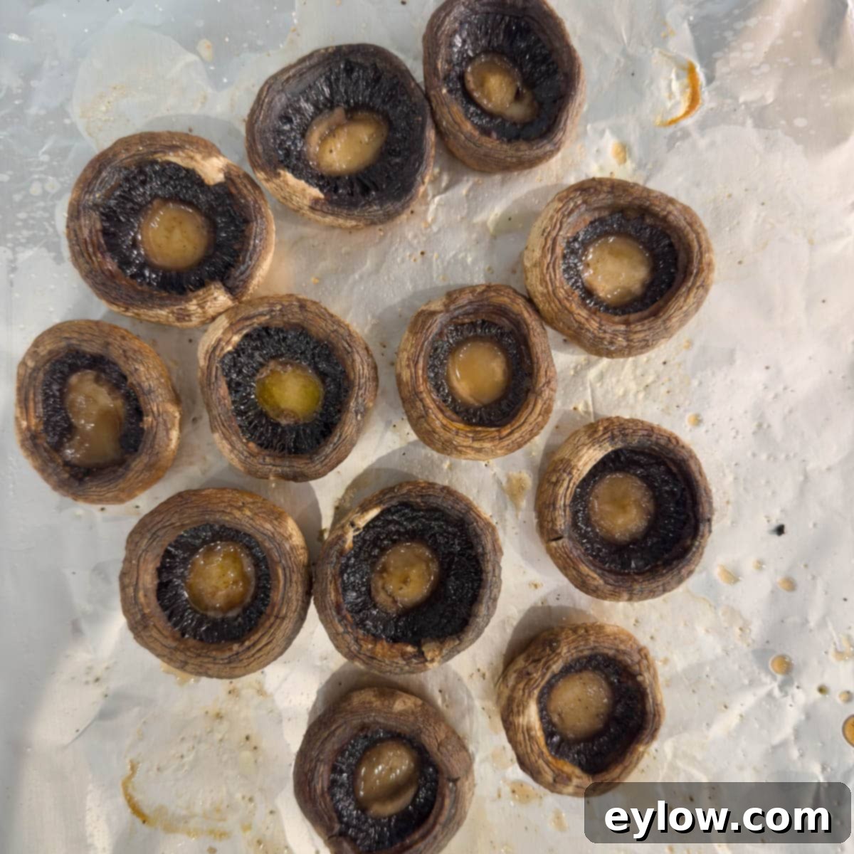 Dark brown, perfectly broiled mushroom caps on a baking sheet, with their natural juices released, ready for stuffing.