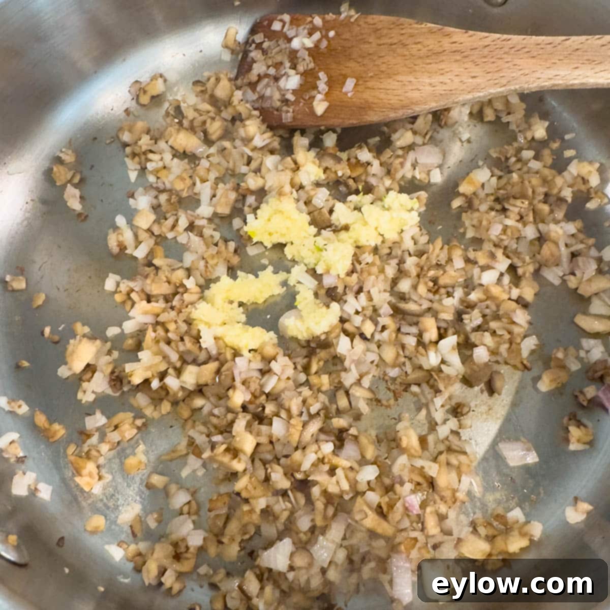 Chopped mushroom stems, shallots, and garlic gently sautéing in a stainless steel pan over medium heat, releasing their aromas.