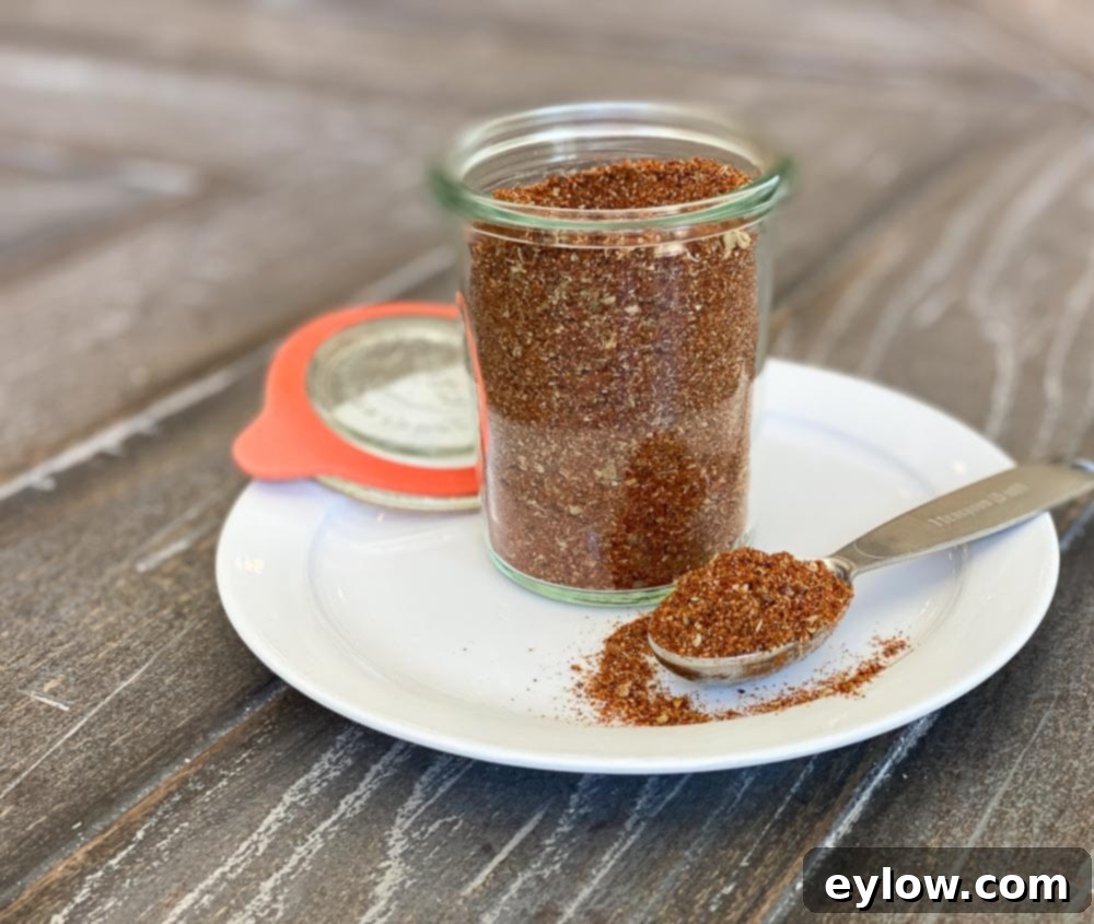 Rusty colored homemade taco seasoning in a jar on a white plate with a tablespoon.