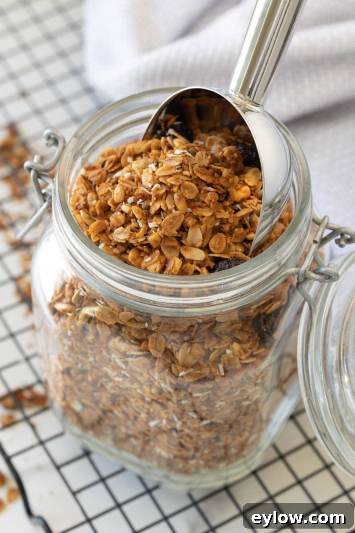 A glass jar of freshly baked homemade granola with a scooper in the top, ready to be enjoyed.