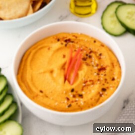 A white bowl of roasted red pepper hummus, beautifully prepared to serve as an appetizer, garnished with a drizzle of olive oil.