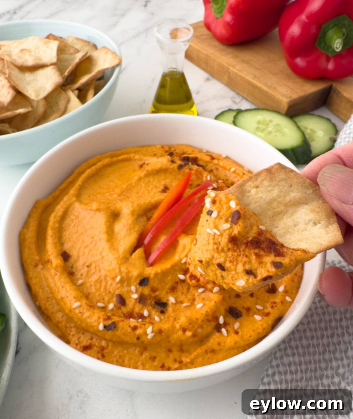 A close-up shot of a single crispy cracker topped generously with a swirl of creamy red pepper hummus, ready to be enjoyed as a delightful appetizer or snack.