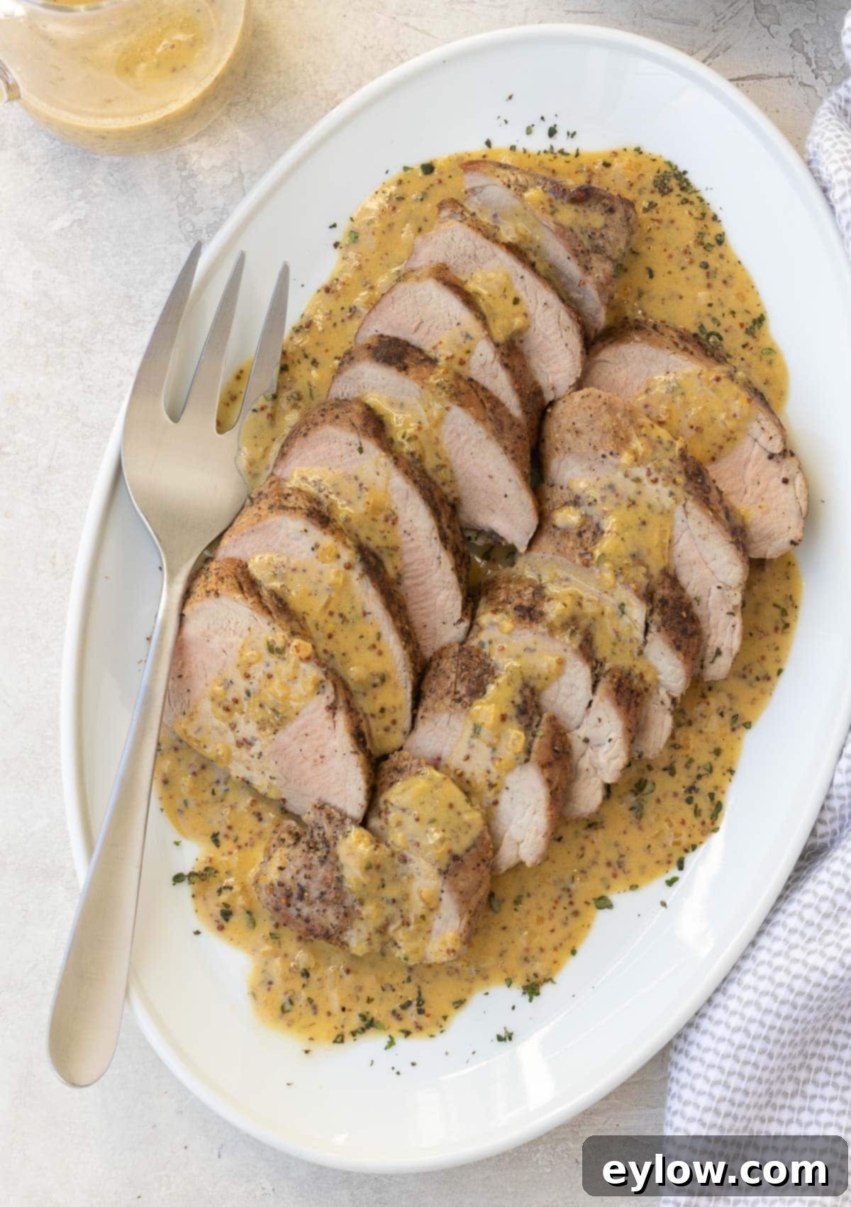 Slices of roast pork tenderloin with a creamy mustard sauce on a white platter. 