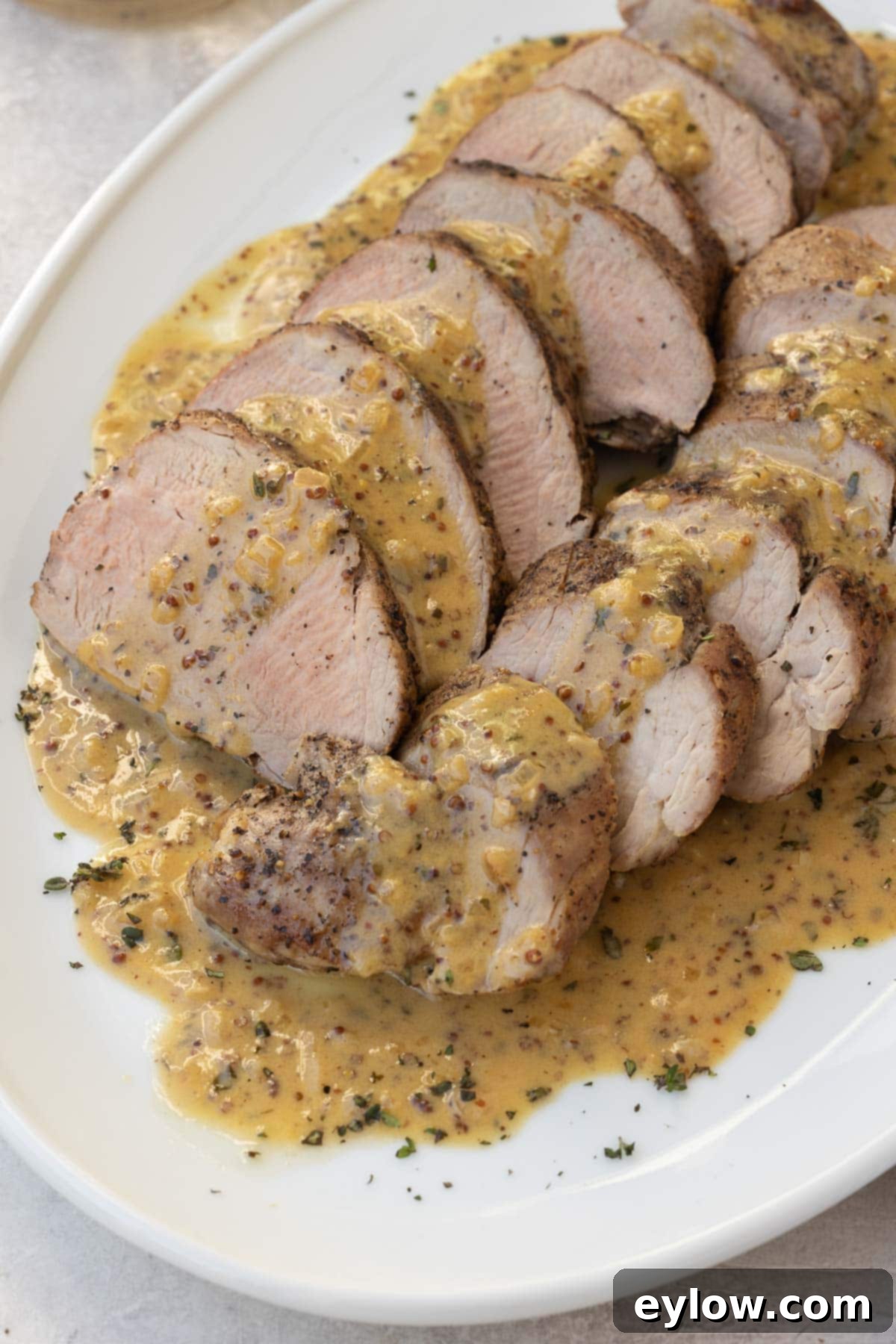 Roast pork sliced for serving on an oval platter with Dijon mustard sauce. 