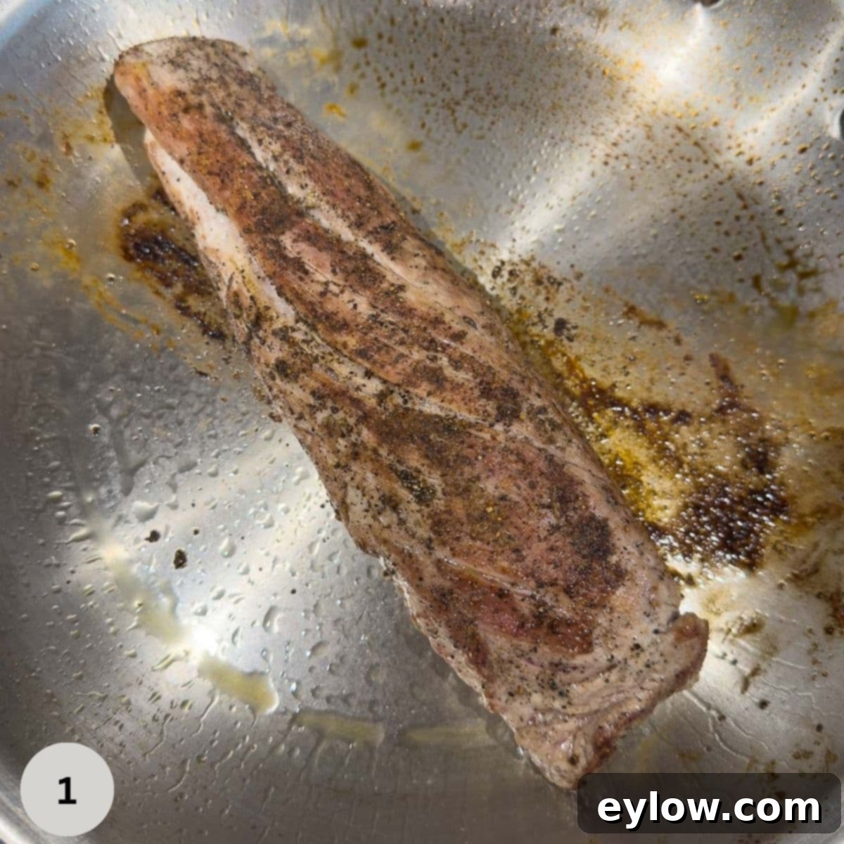 Searing pork tenderloin in a stainless steel fry pan.