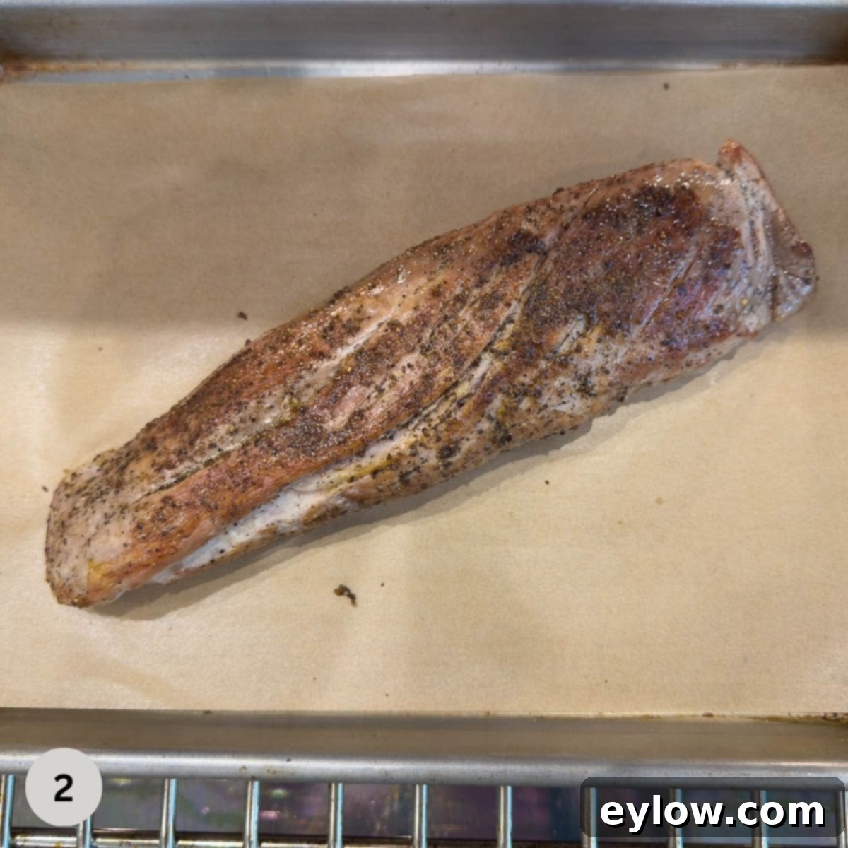 Seared pork tenderloin going into the oven to finish on a sheet tray with parchment.