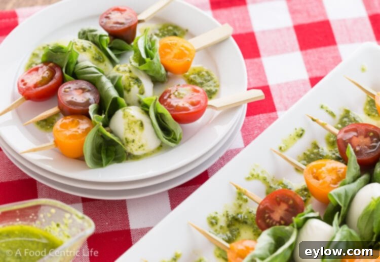 Quick Caprese Bites with Homemade Basil Vinaigrette 5 Skewers on small serving plates with basil vinaigrette, red and white checked tablecloth.