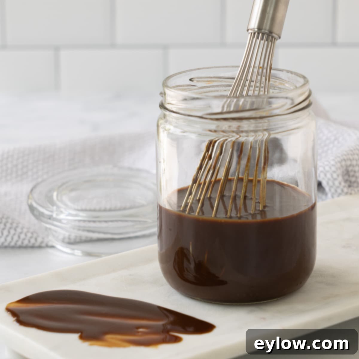 A glass jar with rich brown hoisin sauce and a whisk for mixing.