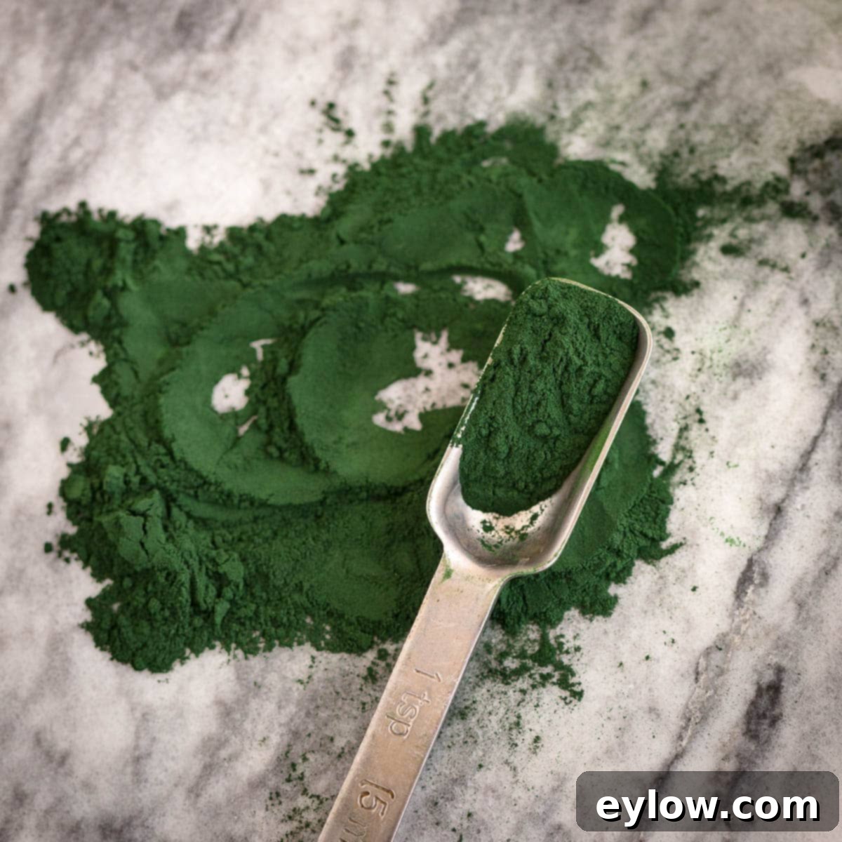 Revitalizing Green Detox Smoothie 5 Deep green spirulina powder on a teaspoon, ready to be added to a smoothie.