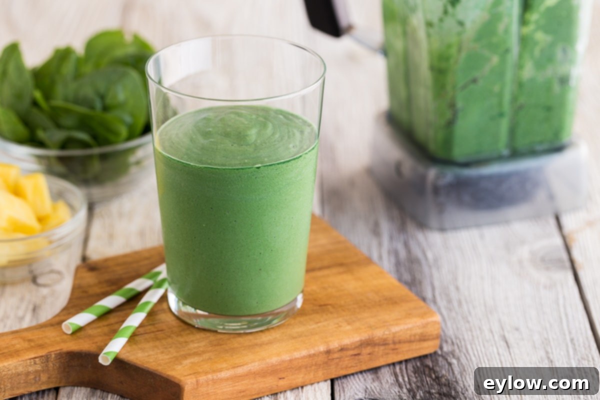 Revitalizing Green Detox Smoothie 6 A bright green detox smoothie in a clear glass with green striped straws on a rustic wooden counter.