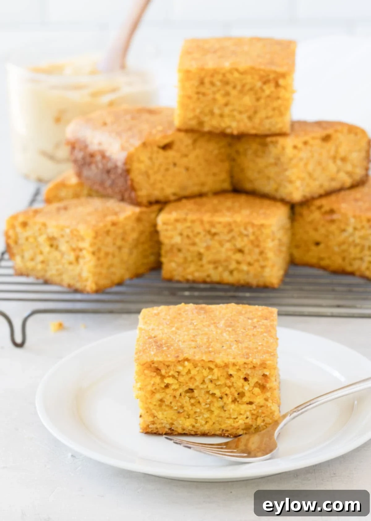 A square piece of golden cornbread with a stack of pieces behind it on a wire rack, showcasing its perfect texture.