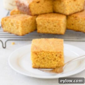 A single piece of gluten-free cornbread on a white plate with silver fork with pieces stacked behind.