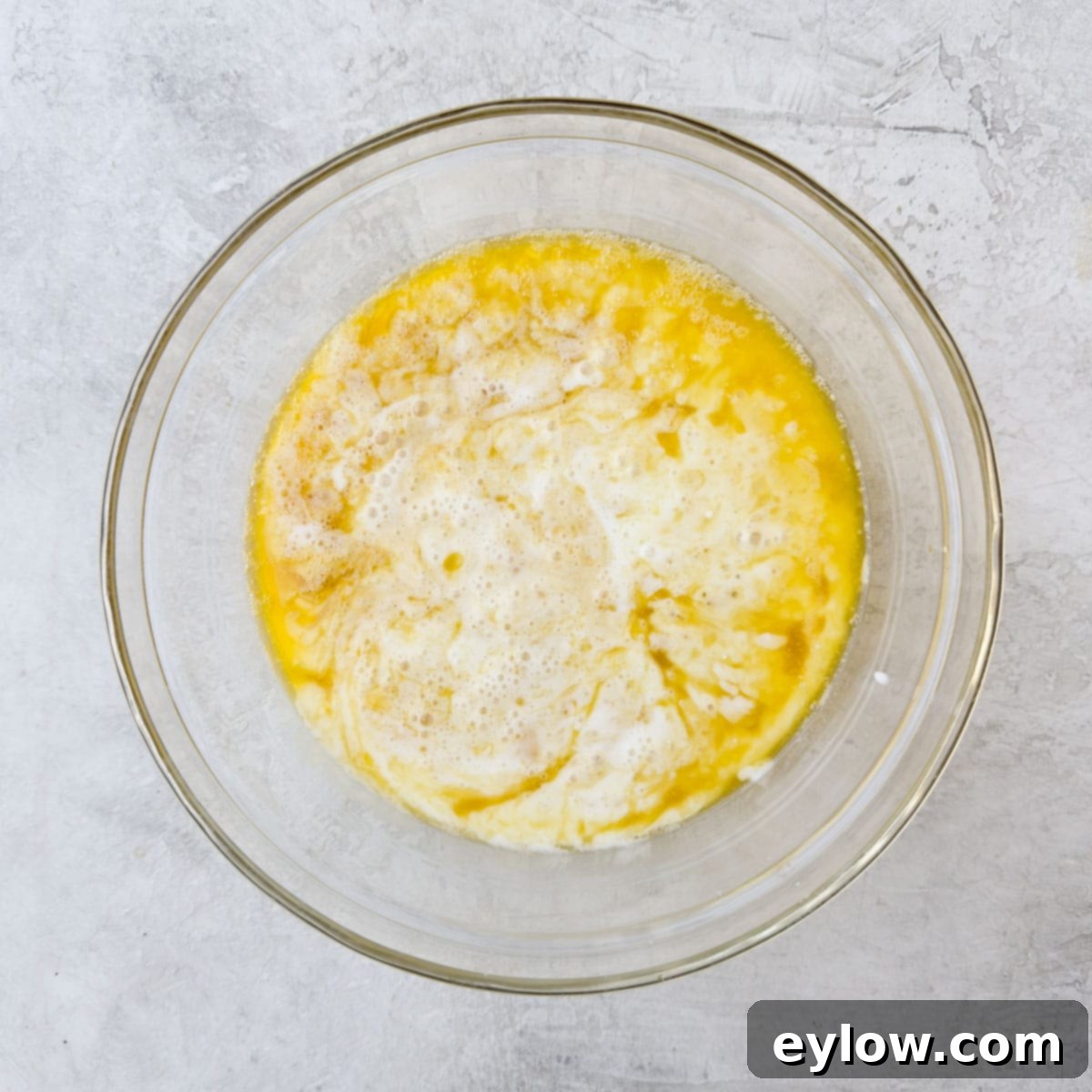 Wet ingredients, including milk, melted butter, honey, and beaten eggs, added to a measuring cup, creating a golden liquid for the cornbread batter.