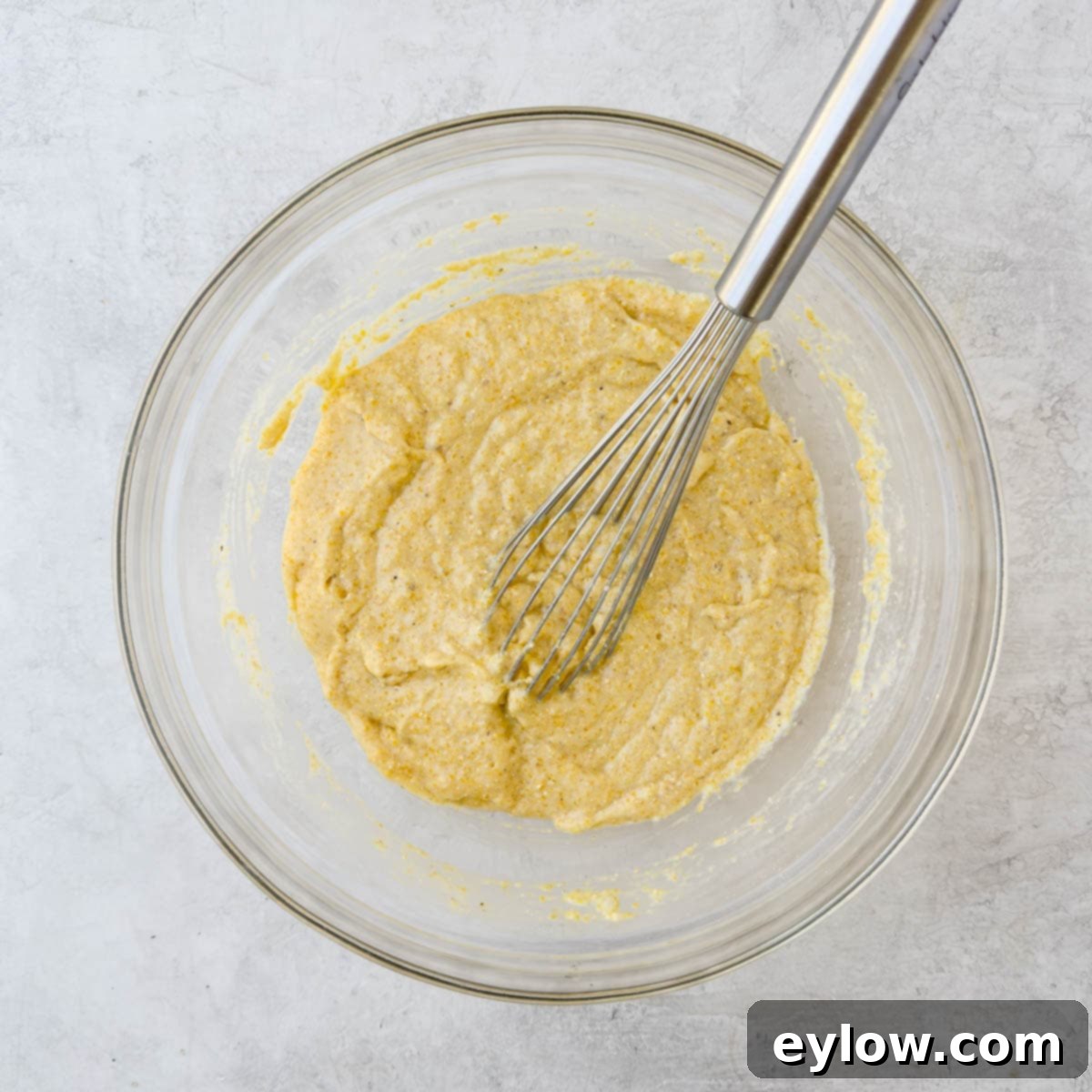 Cornbread batter smoothly whisked together in a glass bowl, showcasing its consistent, creamy texture.