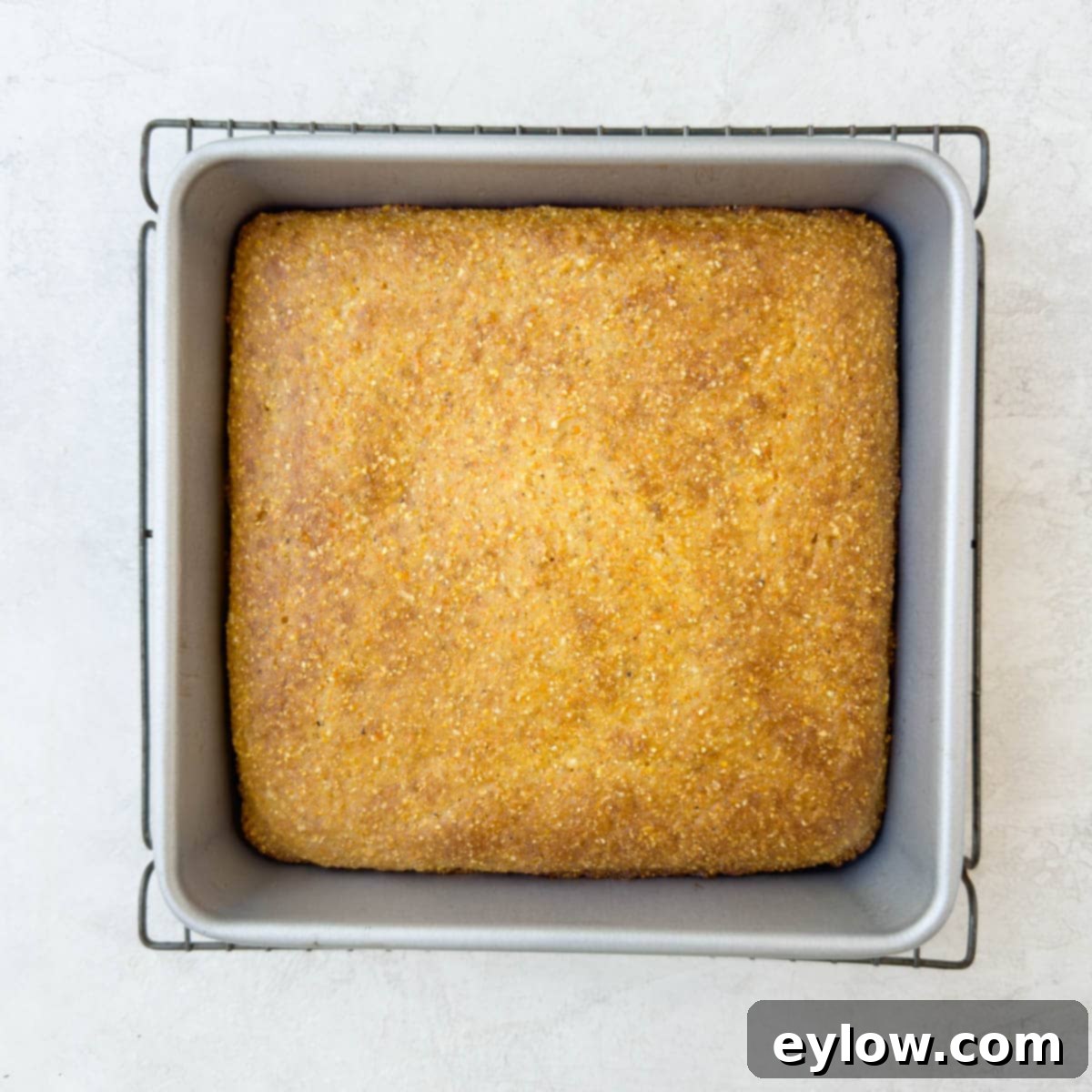 A perfectly baked, golden brown square loaf of cornbread cooling on a wire rack, steam gently rising.
