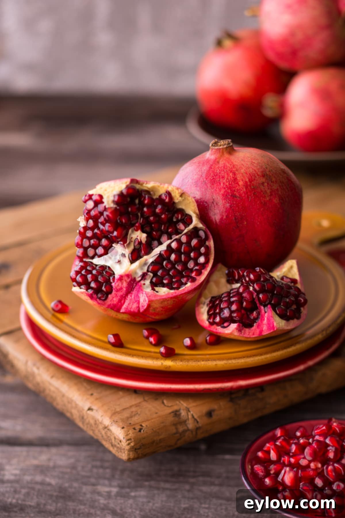 Irresistible Pomegranate Seed Dishes 2 Ruby pomegranates cut open on red and gold plates with small bowl on counter.