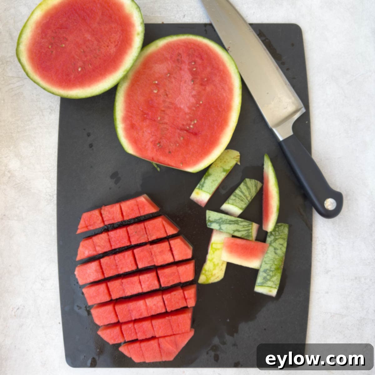 Sweet & Savory Watermelon Basil Feta Salad 5 A sharp knife slicing large watermelon wedges into small, uniform bite-sized cubes on a cutting board.