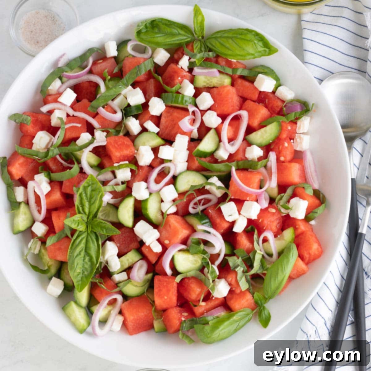 Sweet & Savory Watermelon Basil Feta Salad 10 A beautifully assembled watermelon salad in a glass bowl, showcasing vibrant red watermelon, green cucumber, white feta, basil, and thinly sliced shallots, ready to be served.