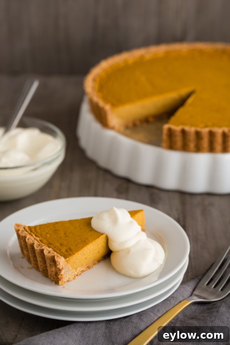 A perfectly sliced piece of gluten-free pumpkin tart on a white plate, topped with a dollop of soft whipped cream, ready to be enjoyed.