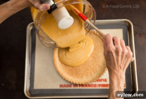 Close-up of creamy pumpkin filling being poured into a baked almond flour tart crust before going into the oven.