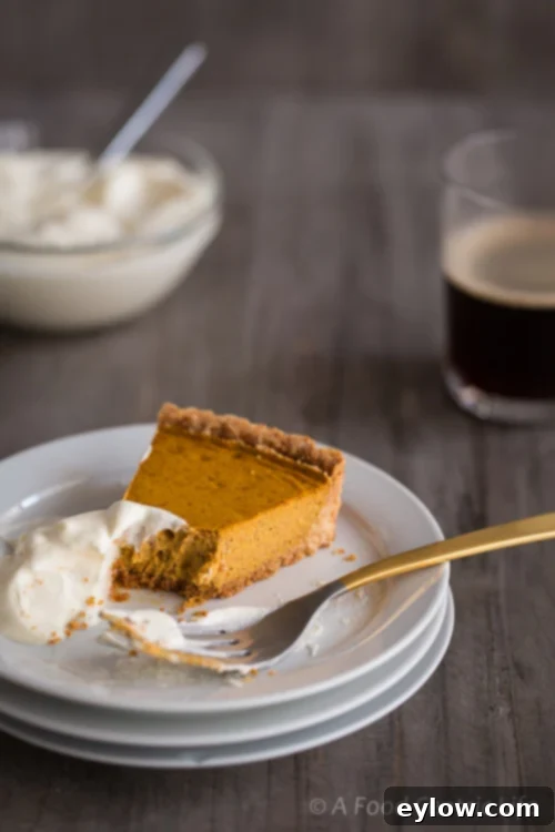 A slice of pumpkin tart with a small bite taken out, accompanied by whipped cream and a cup of coffee, signifying enjoyment.