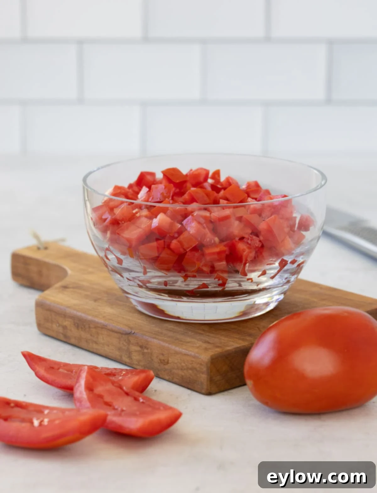 A glass bowl filled with vibrant red diced tomatoes, perfectly cubed and ready for cooking, sits on a kitchen counter.