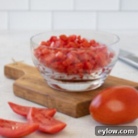 A beautiful glass bowl brimming with perfectly diced tomatoes, showcasing uniformity and freshness, set on a dark cutting board.